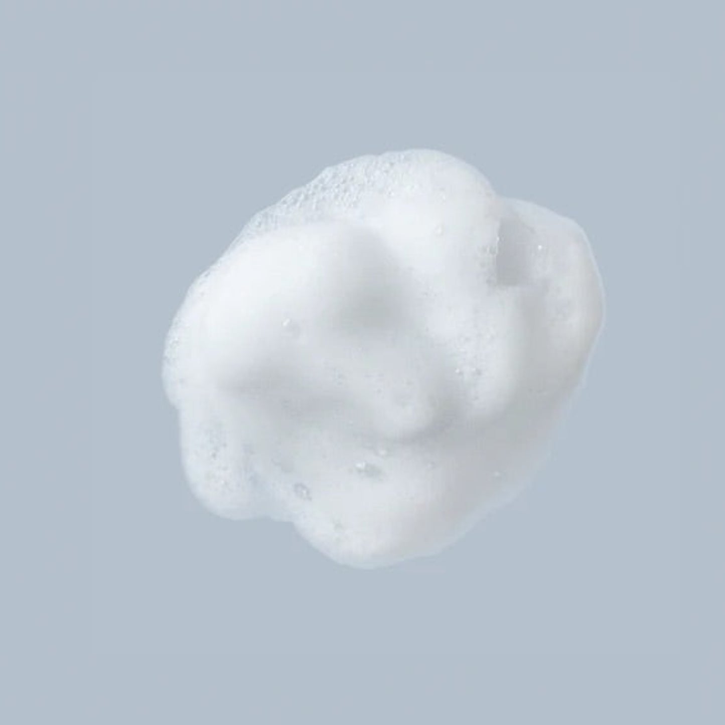 Macro shot of a single dollop of white, creamy Beaver Butter intimate wash foam against a soft grey background.
