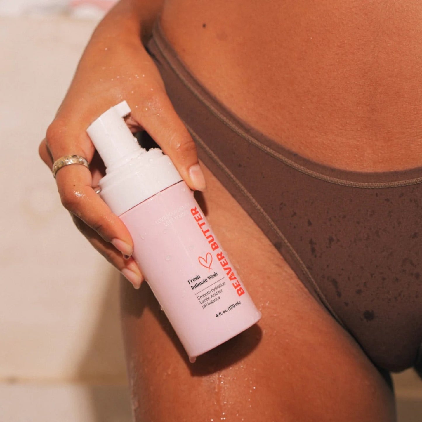 person in brown lingerie holding the Beaver Butter foaming wash bottle against their thigh in a bright, modern bathroom.