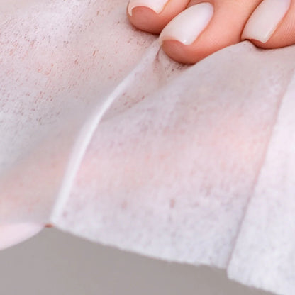 A close-up shot of a person with a clean, neutral manicure holding up a delicate, translucent white intimate wipe, demonstrating the lightweight thickness and soft texture of the material.