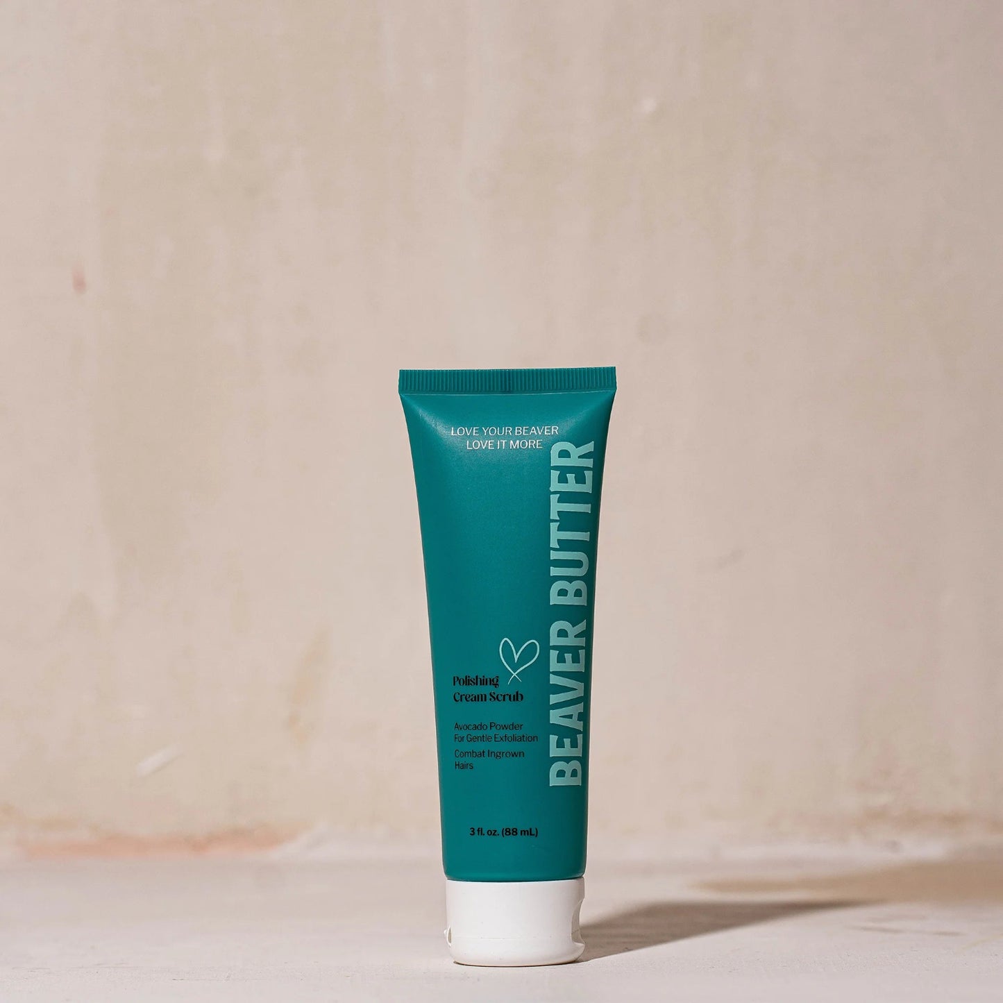 A 3 fl. oz. (88 mL) travel-sized teal tube of Beaver Butter Polishing Cream Scrub standing upright on a minimalist surface against a warm, neutral-toned background.