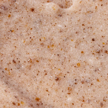 Macro texture shot of the intimate polishing scrub, revealing a beige cream base blended with dark brown and amber natural exfoliating granules for gentle skincare.