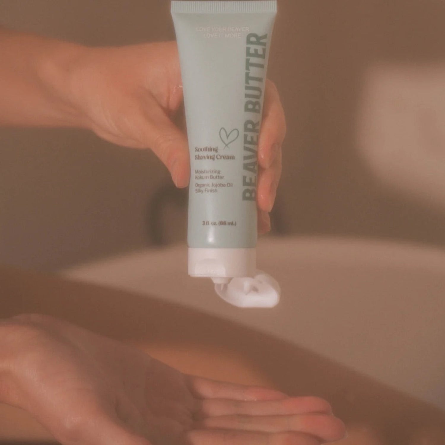 A person's hand dispensing a dollop of white shave butter from the 88ml travel-size teal Beaver Butter tube.