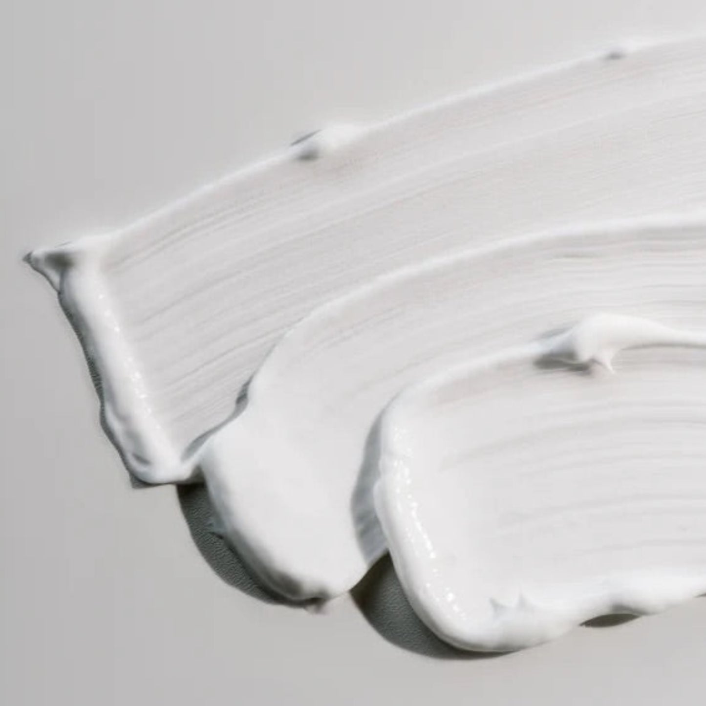 Three smooth, creamy swatches of Beaver Butter Soothing Shave Cream displayed on a neutral grey surface to highlight its rich consistency.