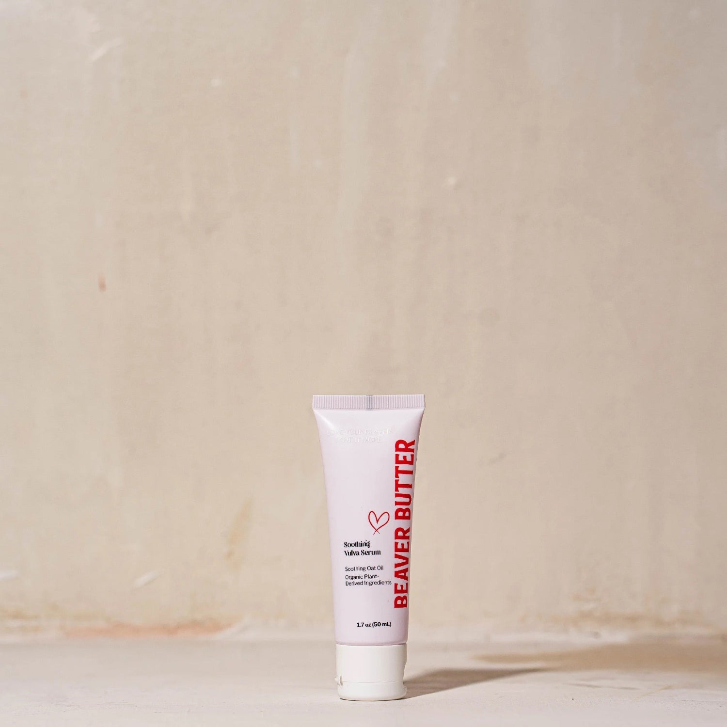 A studio shot of the Beaver Butter Soothing Vulva Serum tube standing upright on a neutral, textured surface with soft lighting.