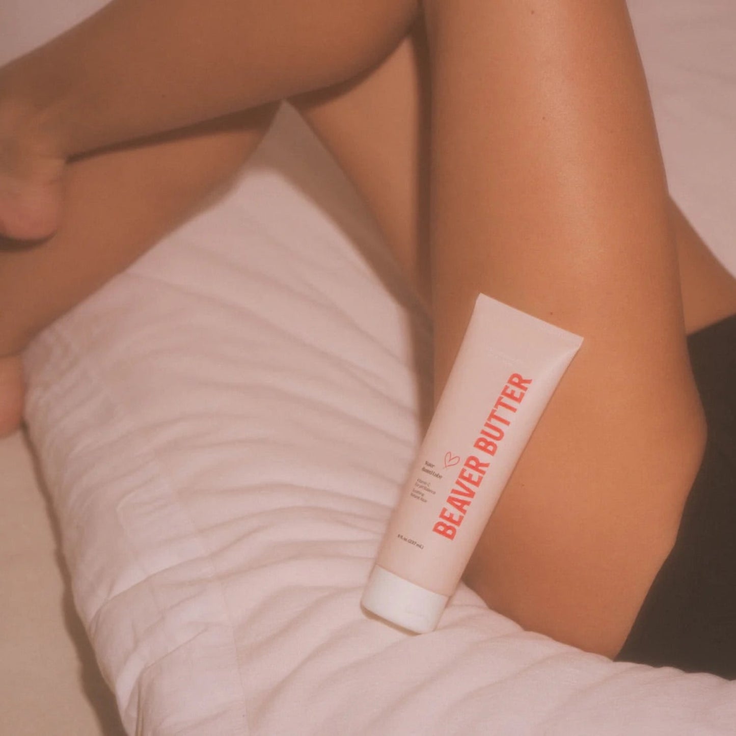 A large 237 ml / 8 fl. oz. tube of Beaver Butter personal lubricant resting on a person's leg in a relaxed bedroom setting.