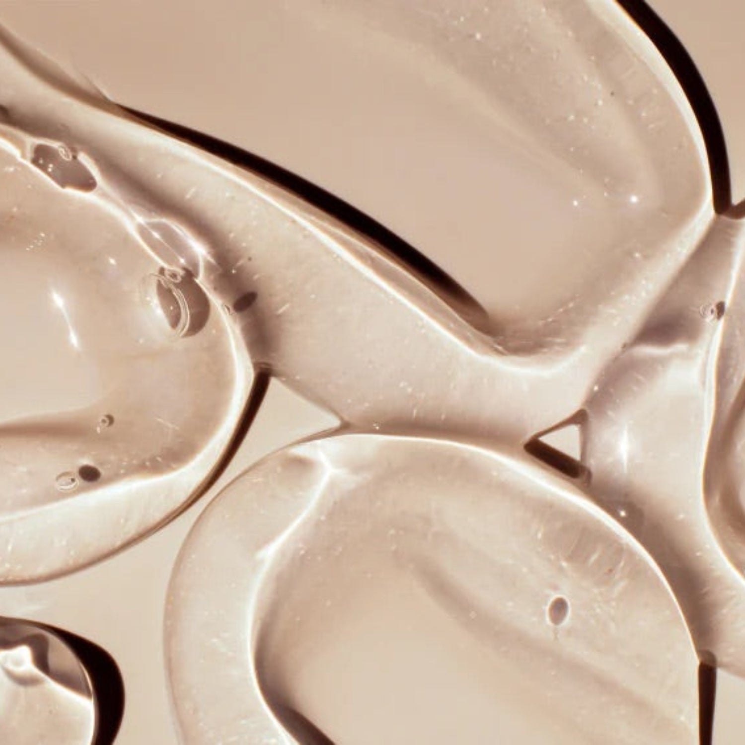 Overhead shot of multiple thick, clear swirls of Beaver Butter water-based lubricant on a neutral tan surface.
