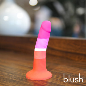 Side view of the blush Avant Pride Beauty Plugs, placed on its suction cup on a wooden surface. On the bottom right corner of the image is the blush logo.