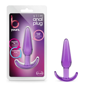 On the left side of the image is the product packaging. On the product packaging (from top): b yours logo, slim anal plug, text bubbles pointing to the product that is visible from the inside the packaging: "body safe phthalate free"; "Tapered tip for easy insertion"; "contoured base conforms to your booty", and in the bottom right is the blush logo. On the right side is the product blush B Yours Slim Anal Plug vertically placed on its base.