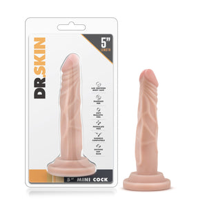On the left side of the image is the product packaging. On the packaging is the Dr. Skin logo, 5" length, product feature icons for: Lab certified body safe; Fragrance free; Soft realistic feel; Phthalate free; Harness compatible; Suction cup base, in the middle is the product visible through clear packaging, and 5" mini cock written in the bottom. Beside the packaging is the product blush Dr. Skin 5" Mini Cock, placed on its suction cup.
