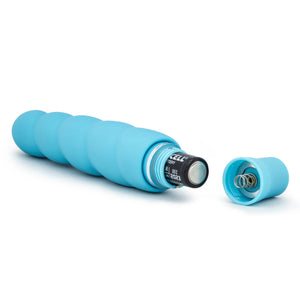 Back side view of the blush Luxe Anastasia Aqua Vibrator, laying on its side, with an open battery cap, and a AA battery sticking out.