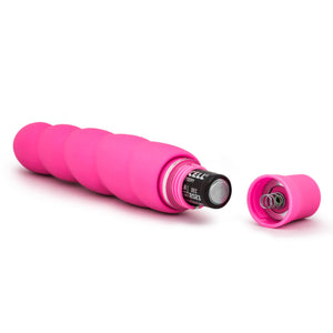 Back side view of the blush Luxe Anastasia Pink Vibrator, laying on its side, with an open battery cap, and a AA battery sticking out.