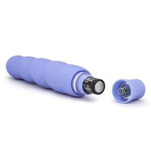 Back side view of the blush Luxe Anastasia Periwinkle Vibrator, laying on its side, with an open battery cap, and a AA battery sticking out.