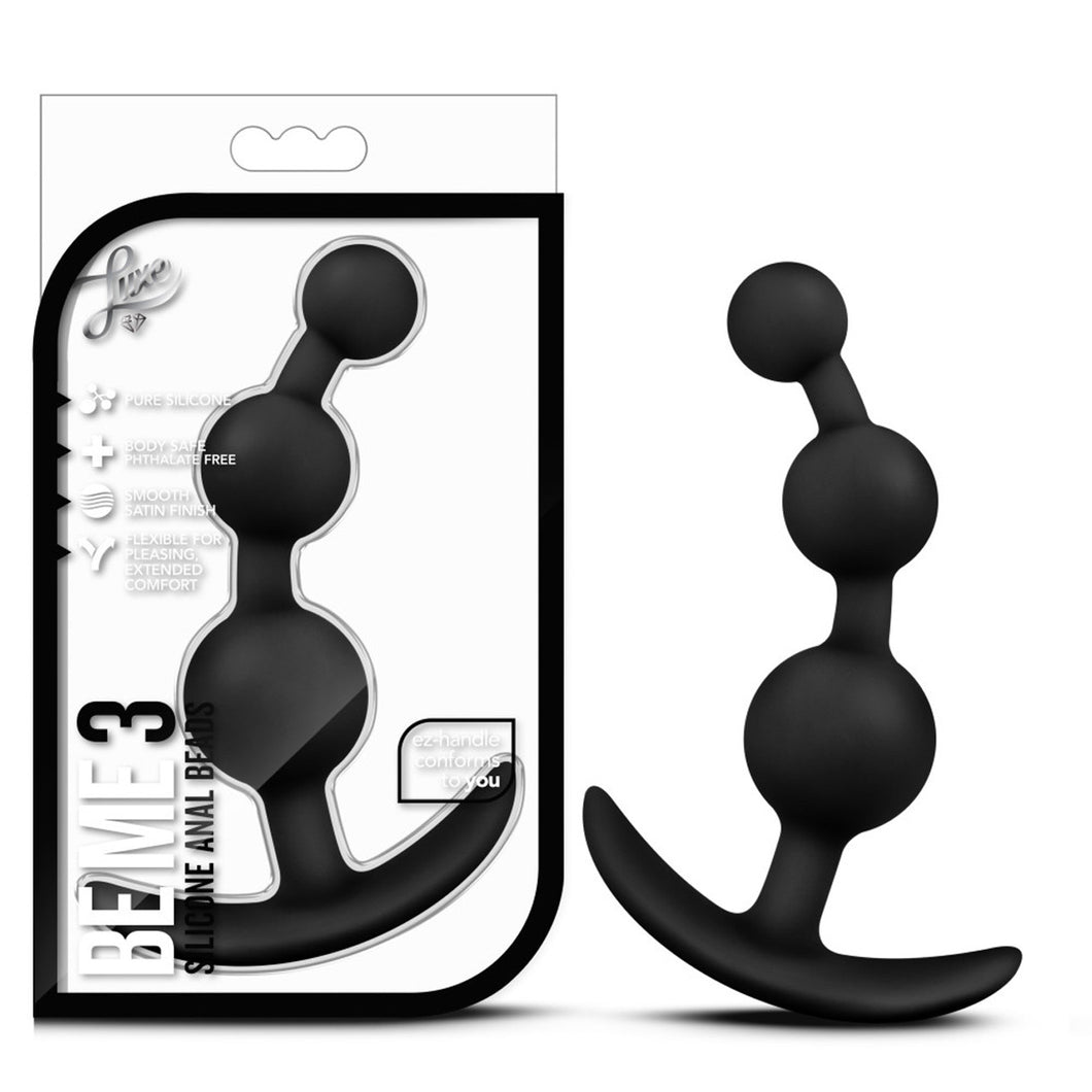 On the left side of the image is the product packaging. On the packing is the Luxe logo, product feature icons for: Pure silicone; Body safe phthalate free; Smooth satin finish; Flexible for pleasing, Extended comfort; ez-handle conforms to you, bottom left side is the product name: Be Me 3 Silicone Anal Beads, and the product inside completely visible through clear packaging. Beside the packaging is the blush Luxe Be Me 3 Silicone Anal Beads, standing on its ez-handle.