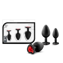 Load image into Gallery viewer, On the left side of the image is the product packaging. On the packaging from the top is the Luxe logo, product name: Bling Plugs Training kit, products completely visible through clear packaging, and product feature icons for: 3 sensual sizes; Platinum cured silicone; Body safe phthalate free; Smooth satin finish. Beside the packaging are the blush Luxe Bling Plugs. The largest plug is laying on its side with the red heart gem facing front, Medium &amp; small plugs are standing from behind.