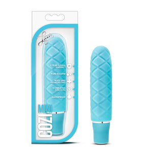 On the left side of the image is the aqua variant product packaging. On the packaging is the Luxe logo, product feature icons for: 5 year global warranty; Pure silicone; Body safe phthalate free; 10 vibrating functions; waterproof, product name: Cozi mini, and the product inside fully visible through clear packaging. Beside the packaging, is the product blush Luxe Cozi Mini Aqua Vibrator, standing up on its base.