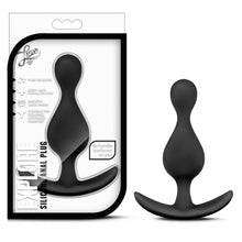 Load image into Gallery viewer, On the left side of the image is the black variant product packaging. On the packaging is the Luxe logo, product feature icons for: Pure silicone; Body safe phthalate free; Smooth satin finish; Flexible for pleasing, extended comfort, ez-handle conforms to you, product name: Explore Silicone Anal Plug, and the black variant of the product inside fully visible through clear packaging. Beside the package is the product blush Luxe Explore Silicone black Anal Plug, stood up on its handle.