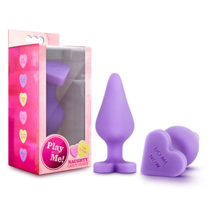 On the left side of the image is the product packaging. On the packaging is a list of different Heart messages: Be Mine; Do Me Now; Spank me; Be Mine; Do Me now; Spank me.  On the front of the package is the product inside displayed through clear packaging, Play with Me! logo, product features: Body safe; Pure silicone, and Product name: Naughty Candy hearts. Beside the packaging are 2 anal plugs, one standing on its base, and the other is laying flat with "Do me now" visible at the bottom of the base.