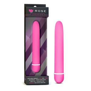 On the left side of the image is the product packaging. On the packaging is the Rose logo, product name: Luxuriate, the pink variant of the product inside visible through clear packaging, and product features at the bottom: 1 YEAR GLOBAL WARRANTY; QUIET AND DISCREET; WATERPROOF; SMOOTH SATIN FINISH; BODY SAFE; PHTHALATE FREE; POWERFUL MULTISPEED VIBRATIONS. Beside the packaging is the product, blush Rose Luxuriate pink Vibrator, standing on the bottom of its cap.