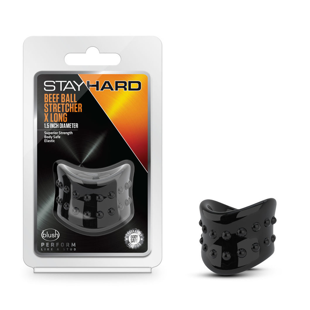 On the left side of the image is the product packaging. On the packaging is the Stay Hard logo, product name: Beef Ball Stretcher X Long 1.5 Inch Diameter, product features: Superior Strength; Body Safe; Elastic, the product inside visible through clear packaging, blush logo, slogan: Perform like a stud, and an icon for Body safe - Laboratory certified. Beside the packaging is the product blush Stay Hard Beef Ball Stretcher X Long - 1.5 Inch Diameter.