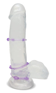 Side view of a clear dildo standing on its suction cup base, with 3 blush Stay Hard Beaded Cock Rings wrapped around the middle of the shaft, at the base of the shaft, and at the base of the dildo, above the suction cup. Showing the placements of the Cock Rings.