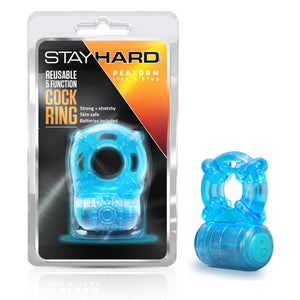 On the left side of the image is the product packaging. On the packaging is the Stay Hard logo, "Premium like a stud", Product name: Reusable 5 function Cock Ring, product features: Strong + stretchy; Skin safe; Batteries included, and below is the product inside visible through clear packaging. Beside the packaging is the product blush Stay Hard Reusable 5 Functions Cock Ring.