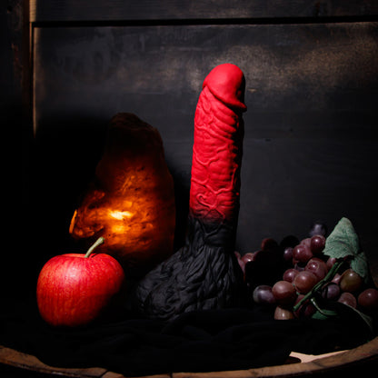 Side view of the blush The Realm Lycan Lock On Dildo standing on its base beside an apple, and a bushel of grapes.