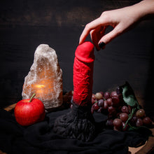 Charger l&#39;image dans la galerie, Side view of the blush The Realm Lycan Lock On Dildo, standing on its base beside an Apple, and a bushel of grapes, with a female&#39;s hand reaching down, and gently touching the tip of the dildo.