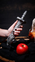 Load image into Gallery viewer, A close up of a female&#39;s hand lifting the blush The Realm Rougarou, with an apple laying on top of a dark cloth covering a barrel like object.