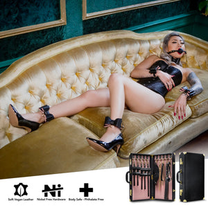 A woman laying on a couch, wearing a ball gag with ankle and wrist restraints on her, without the chains. At the bottom, feature icons for: Soft vegan leather; Nickel free hardware; Body safe- phthalate free, and on bottom right is the suitcase open & closed.
