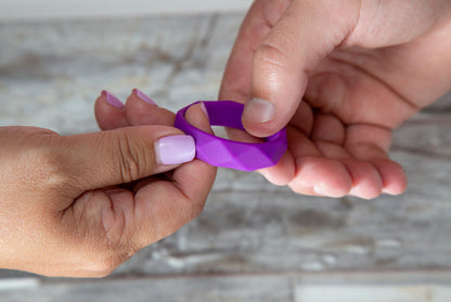 Close up of woman's hands handing the blush Wellness Geo Silicone C-Ring as a man's hand is receiving it from the other side.