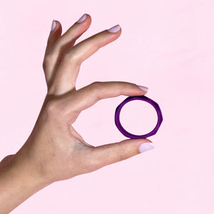 Female's hand showing the side of the blush Wellness Geo Silicone C-Ring by holding it with 2 fingers at the top and bottom.