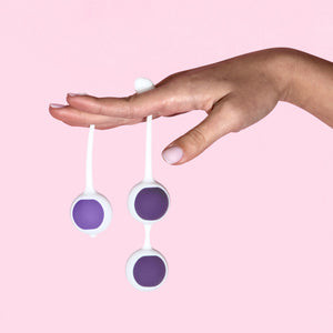 A females is holding the single with a 36.9 gram / 1.3 oz snapped in, and a double with two 51 gram / 1.8 ounce kegel balls snapped in, with her fingers, and palm facing down.