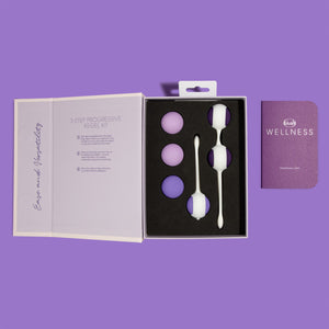 Top down view looking at the opened packaging of the blush Wellness Kegel Kit. On the side flap "Ease and Versatility", on the main cover "3-Step Progressive Kegel Kit", with 3 steps of instructions printed below. In the main part of packaging are the three Kegel balls (2 17g / 0.6 oz & 1 36.9 g / 1.3 oz) nested individually, in a single holder is clipped in the 2nd 36.9 g / 1.3 oz kegel balls, and in a double nested holder are the 2 51 g / 1.8 oz Kegel Balls. Beside the packaging is the Wellness guidebook.