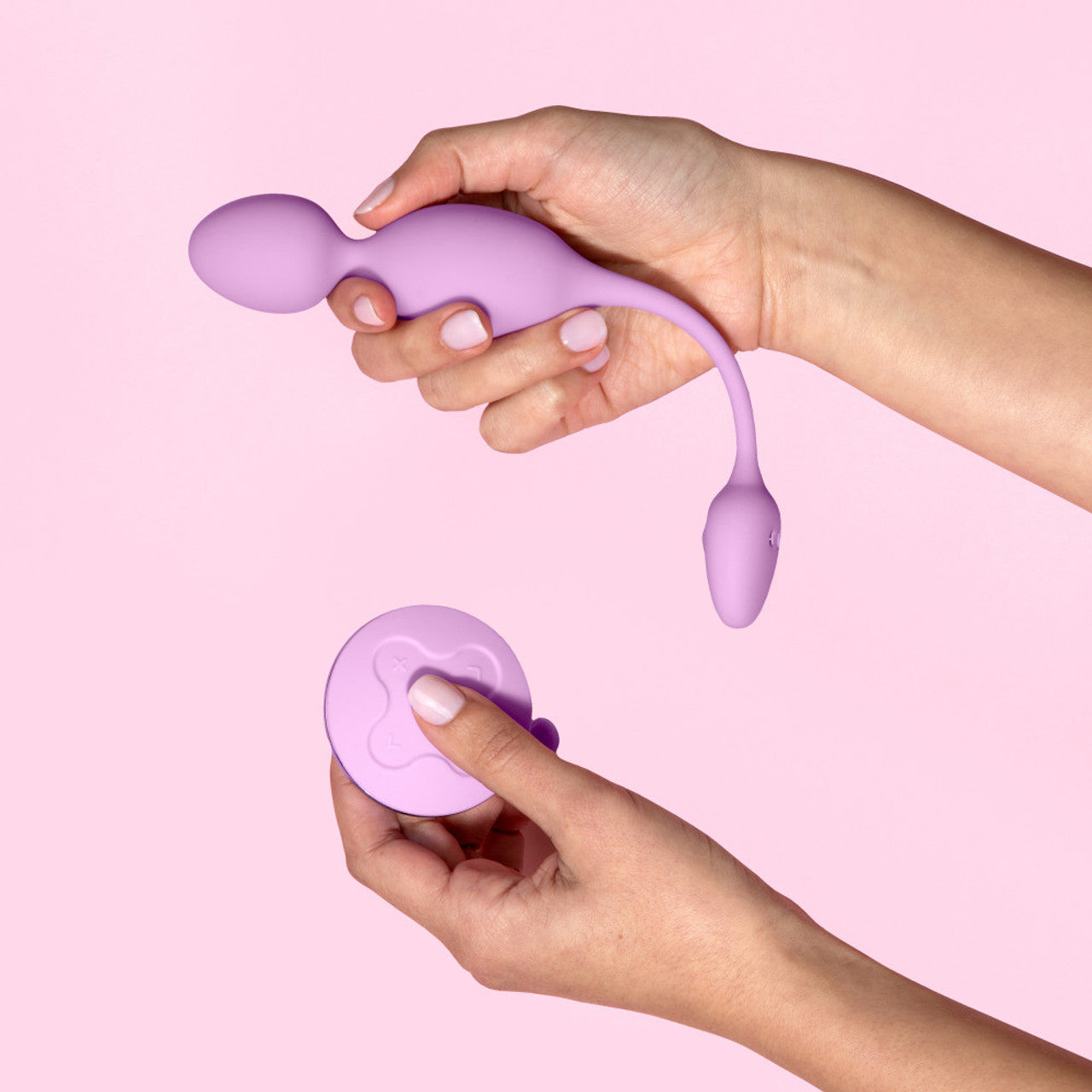 Close up at female's hand holding the blush Wellness Raine Vibrating Kegel Ball in her right hand, thats parallel and slightly above her left hand that's holding the wireless control.