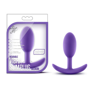 On the left side of the image is the product packaging. On the packaging is the luxe logo, product feature icons for: Wearable; Pure silicone; Tingly vibrations; Hypoallergenic; Smooth satin finish; Comfortable anchor base, product name: Wearable Vibra Slim plug Medium, and the product fully visible inside the clear packaging. Beside the packaging, is the product, blush Luxe Wearable Vibra Slim Plug stood up on its handle.
