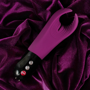 Fun Factory Jewels MANTA Limited Edition Penis Toy laying on purple velvety fabric, on the products handle are visible control buttons, and the Fun Factory logo.