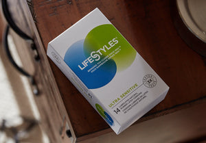 A box of LifeStyles Ultra Sensitive 14 Lubricated Natural Rubber Latex Condoms, laying on top of a night stand.