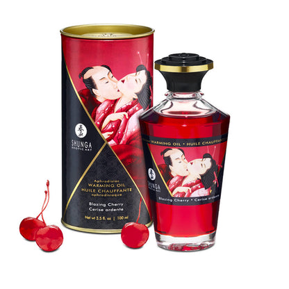 Shunga Blazing Cherry Warming Oil bottle and its decorative red storage tin, displayed with fresh cherries to highlight the edible flavour.