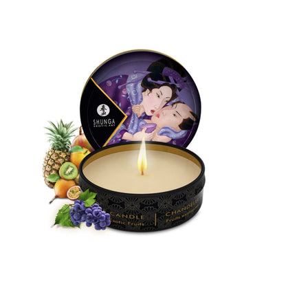 A 30ml SHUNGA LIBIDO massage candle in a black tin, lit to show a flickering flame, surrounded by tropical fruits like pineapple and kiwi.