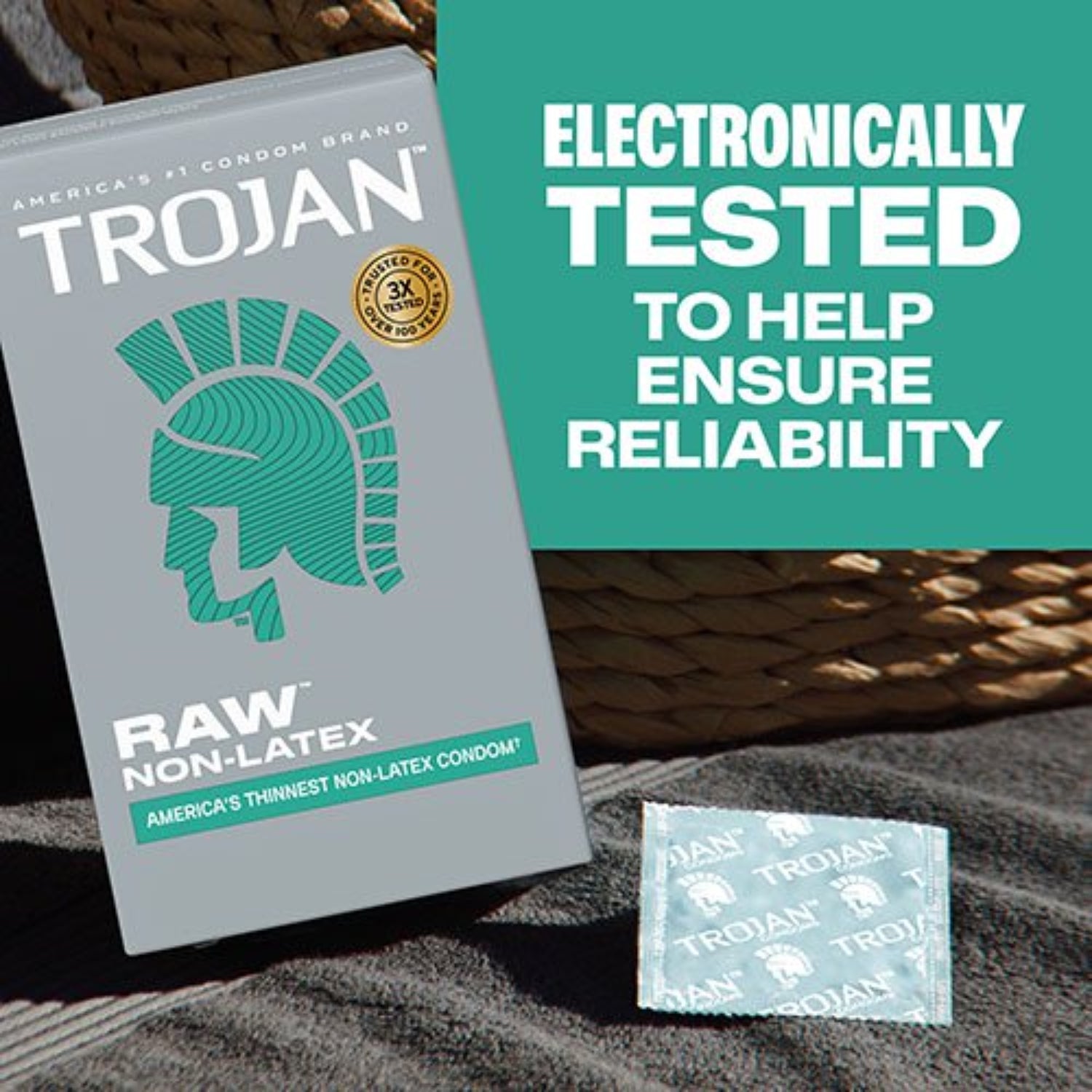 Grey box of Trojan Raw Non-Latex condoms sitting next to an individually wrapped square foil condom wrapper on a dark grey towel.