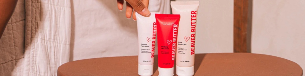 Three tubes of Beaver Butter on a wooden surface with a blurred background