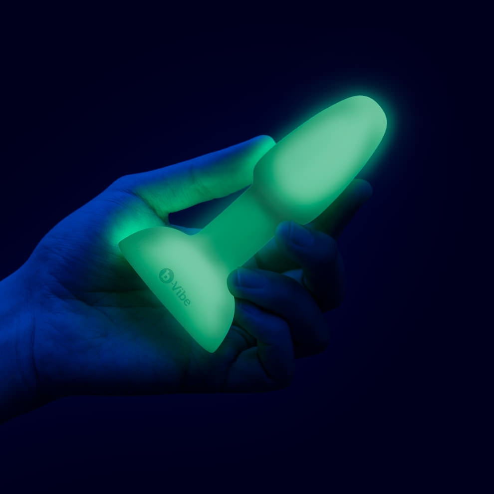 b-Vibe Asstronaut Glow-In-The-Dark Rimming Plug held showing the size scale of the product while glowing i the dark