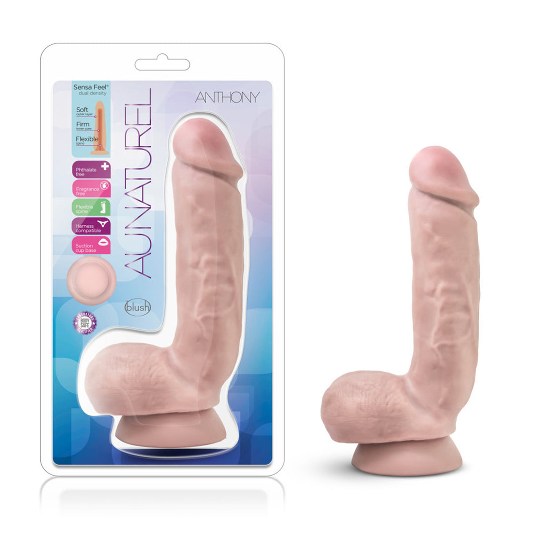 On the left side of the image is the packaging for the product. On the package is written (left to right): Sensa Feel dual density: Soft outer layer; Firm inner core; Flexible spine. Phthalate free; Fragrance free; Flexible spine; Harness compatible; Suction Cup base; Laboratory Certified body safe. Au Naturel blush Anthony. On the right side of the image is the product blush Au Naturel Anthony side view, placed on the suction cup.