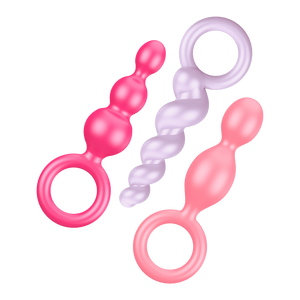 Satisfyer Booty Call Plugs Coloured variant, placed flat diagonally. Top to Bottom one pink plug, upside down light purple plug, and a light pink plug.